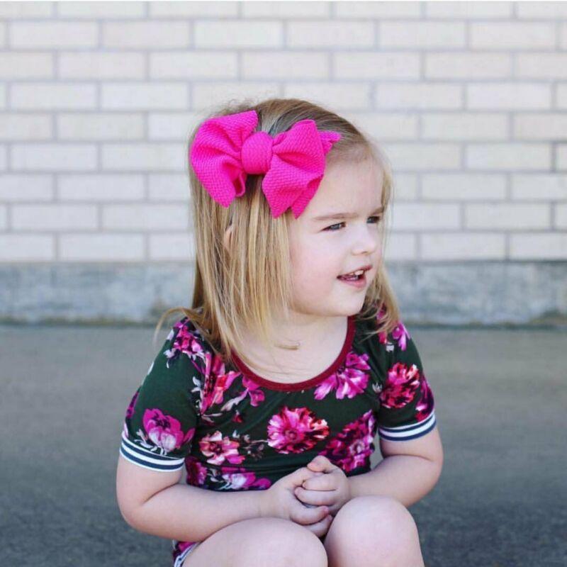 Young girl with pink bows in her hair sitting against a brick wall. Little Janey Shop