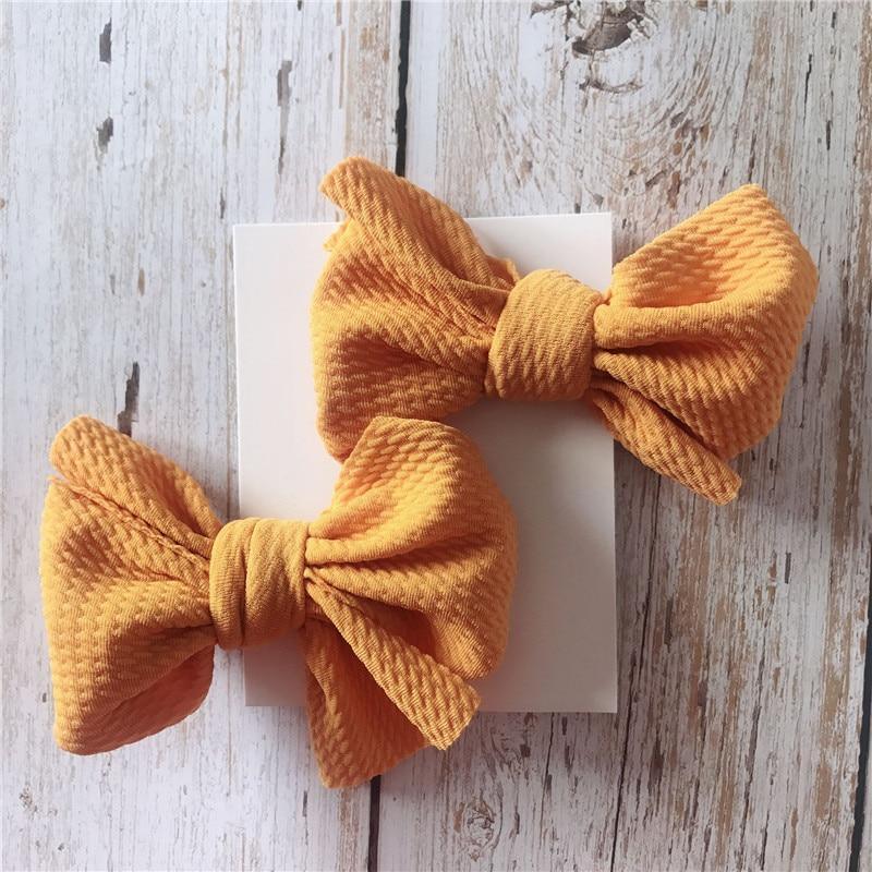 Two mustard yellow textured Handmade Grosgrain Hair Bow Clips on a white card with a wooden background. Little Janey Shop