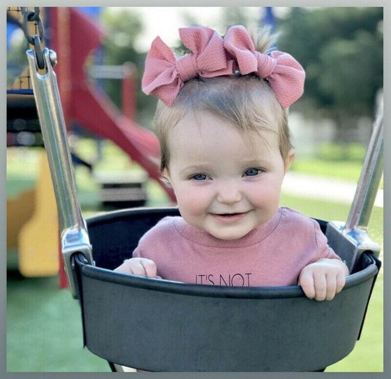 Child in a swing with pink bows and a pink shirt at a playground. Little Janey Shop