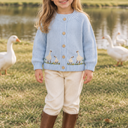 Girl wearing the goose cardigan and riding boots beside geese near a farm pond