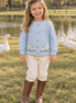 Girl wearing the goose cardigan and riding boots beside geese near a farm pond
